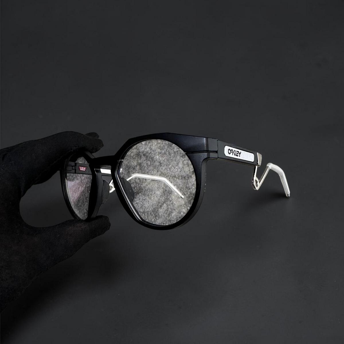 Gafas OakGlasses HSTN Metal con montura negra redonda y patillas blancas sobre fondo gris