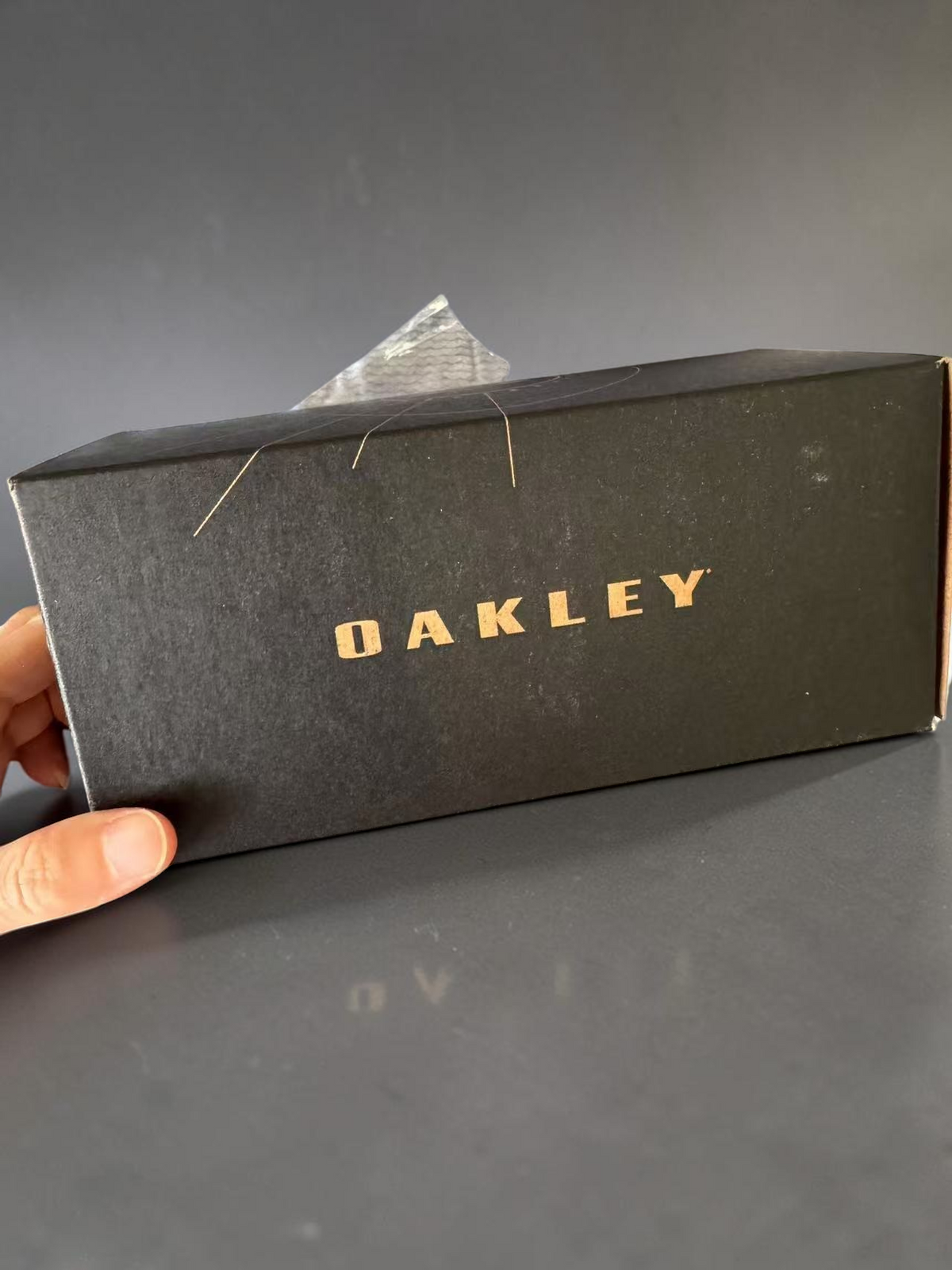 Caja negra de OakGlasses para gafas BXTR Metal con el logotipo de la marca en letras doradas sobre fondo texturizado