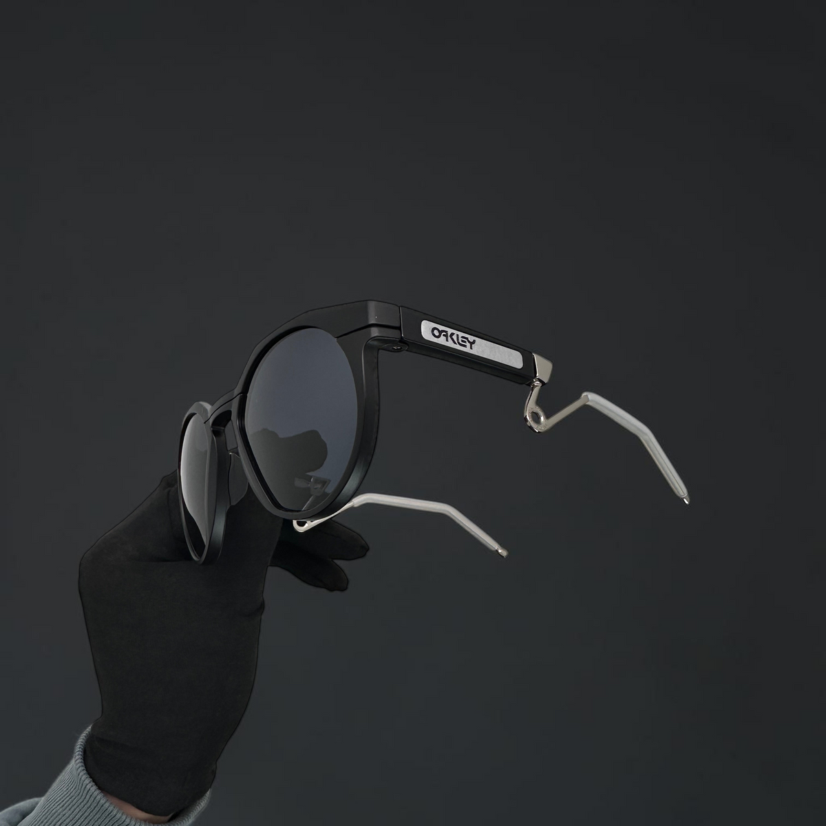 Gafas de sol OakGlasses HSTN Metal con montura negra mate y varillas de metal plateado en mano con guante negro